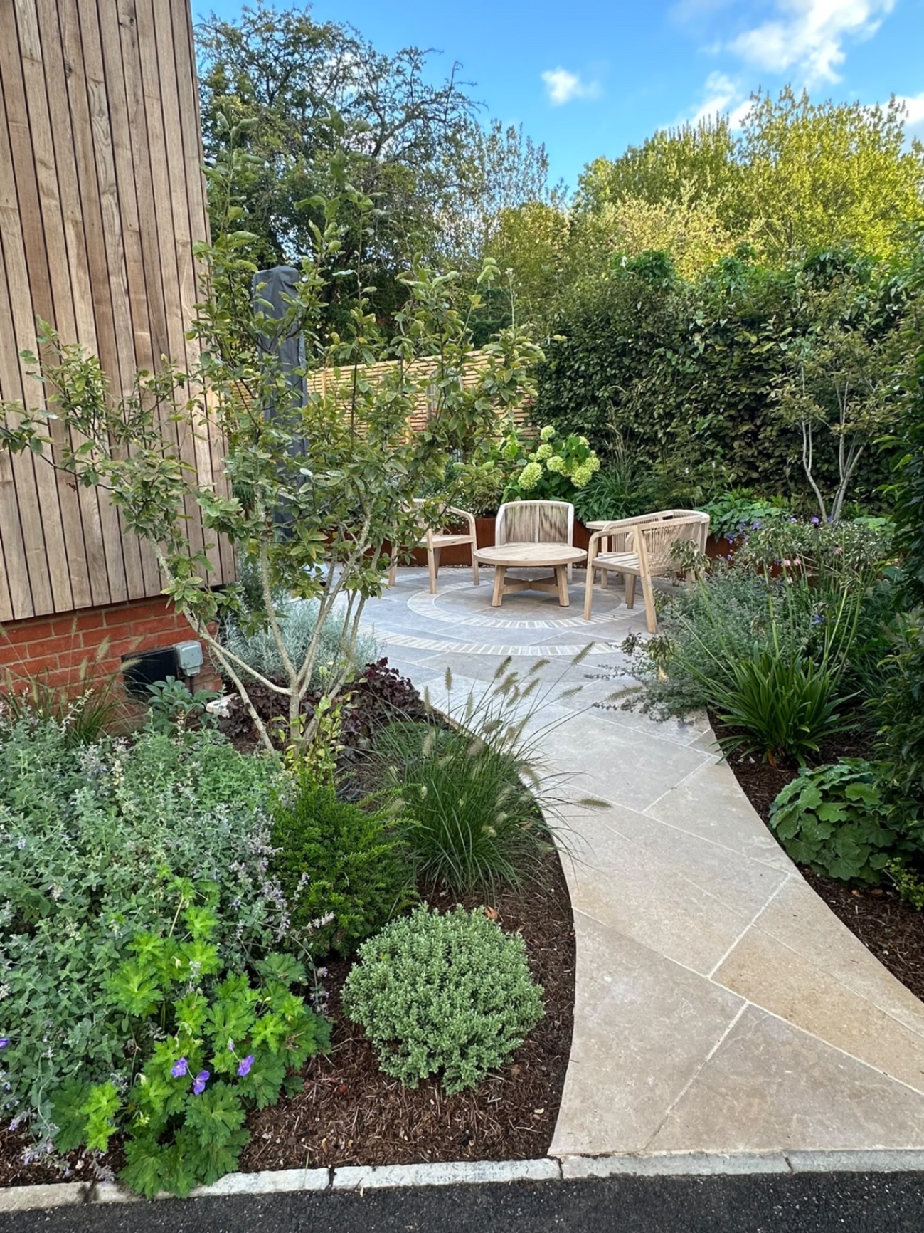 Curved limestone path leading to a circular seating patio framed by a corten steel retaining wall