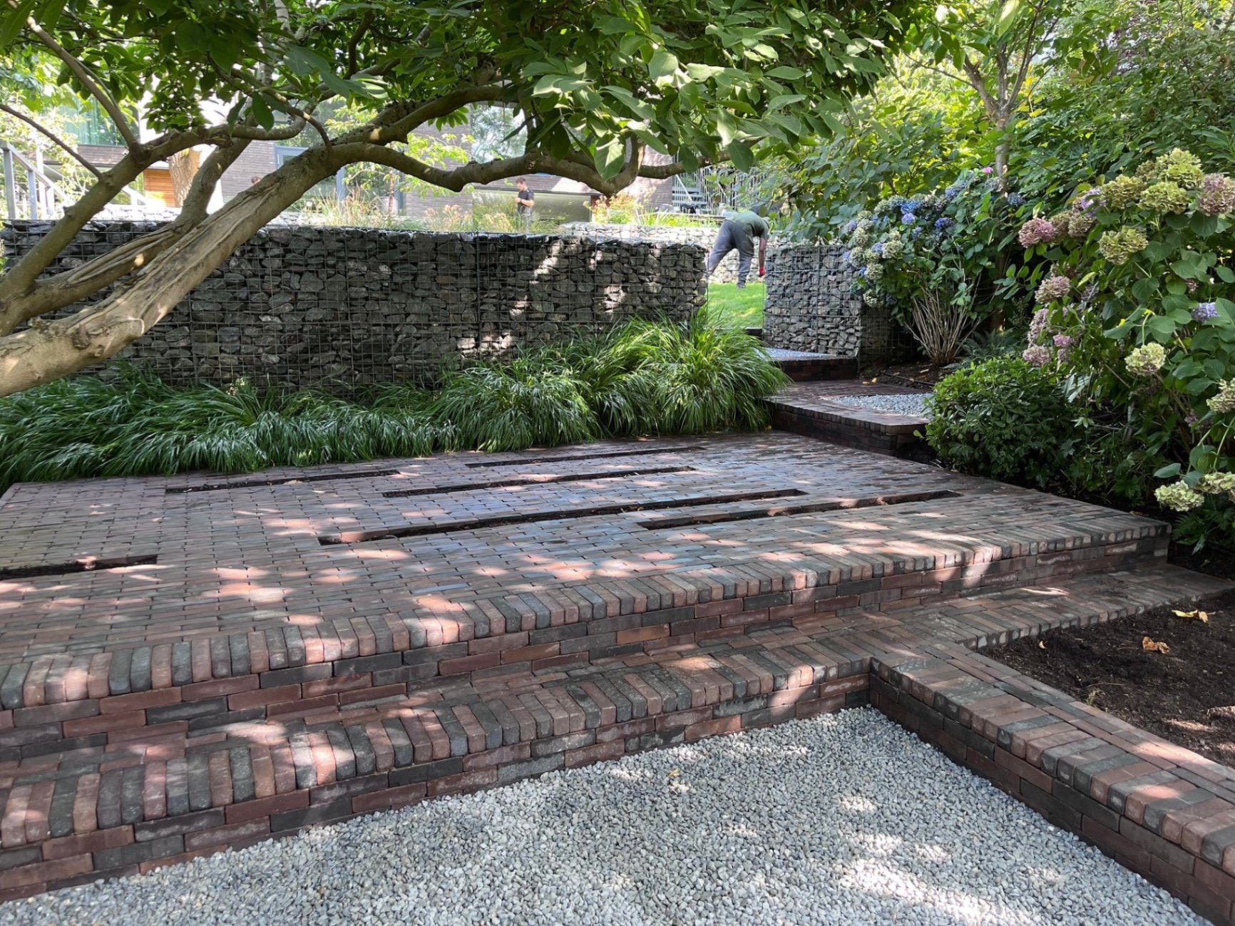 Clay pavior steps rising from a gravel area up the slope beside a gabion retaining wall