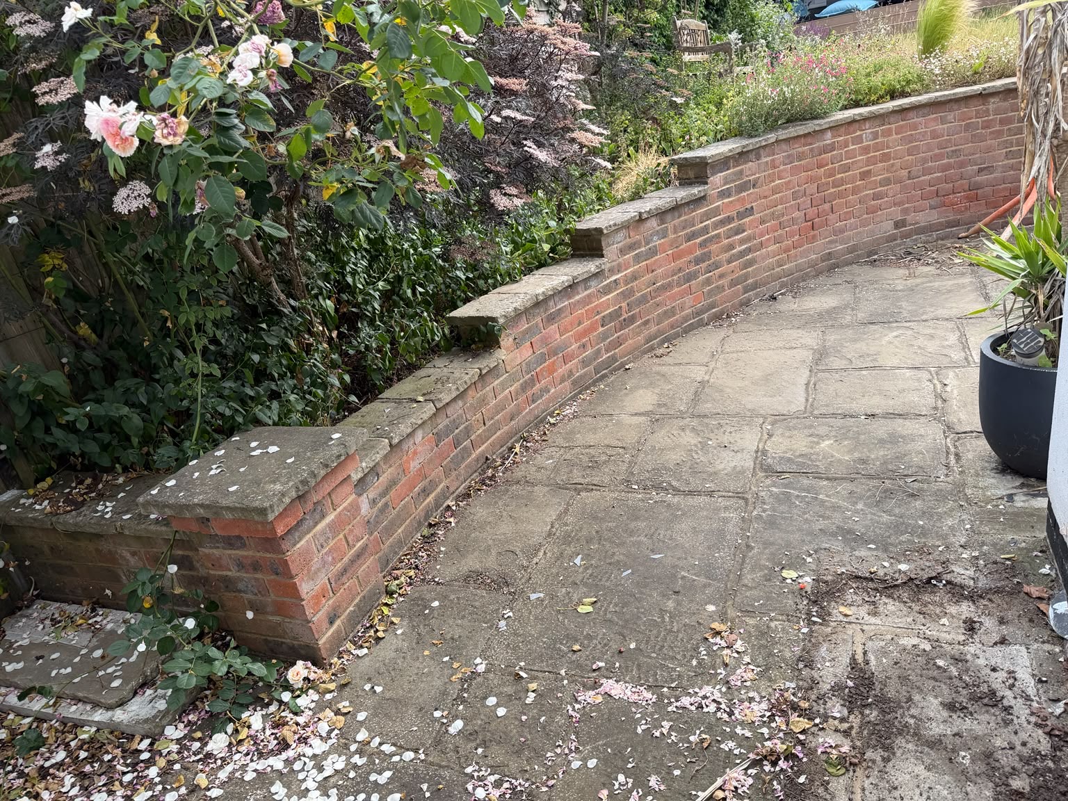 Original curved brick retaining wall and weathered paving before the transformation
