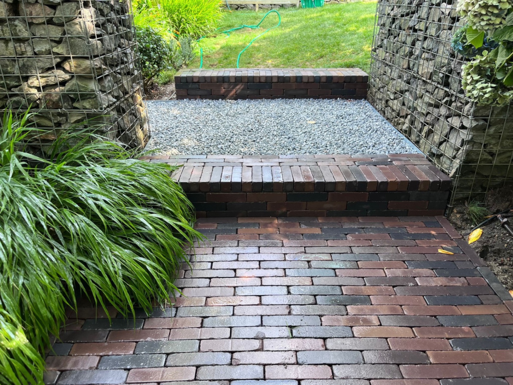 Clay pavior steps with a gravel landing between them and metal edging, flanked by two gabion structures leading toward the lawn