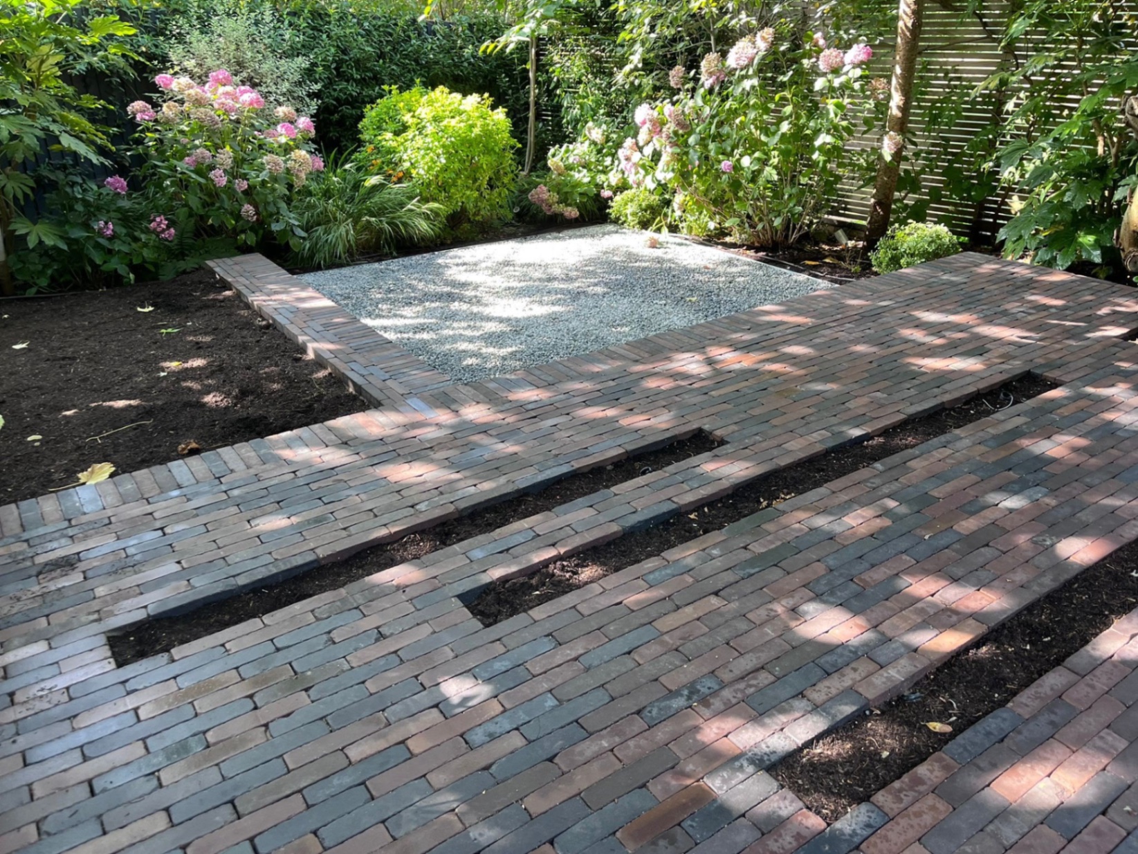 Clay pavior terrace with three unplanted rectangular planting inserts and a square gravel landing, before planting was installed