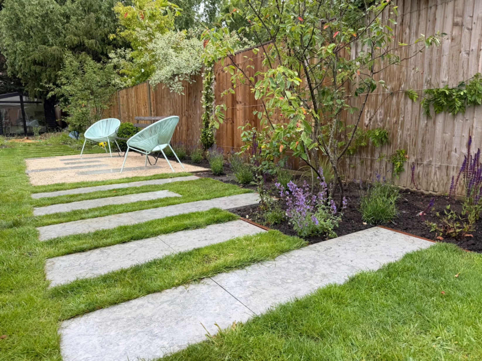 Low-angle view along the stepping-stone path to a gravel seating area with aqua chairs