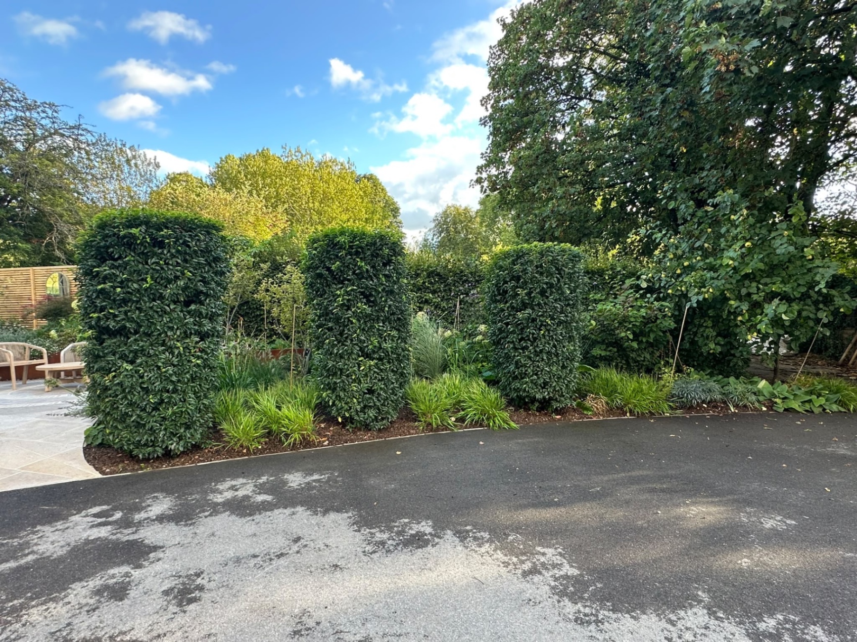 View across the driveway toward three clipped pillar hedges and the circular garden mirror