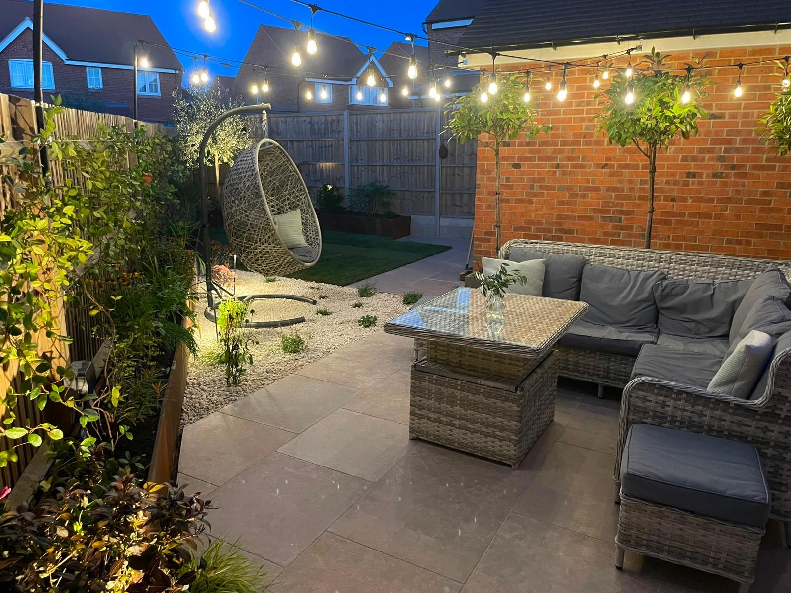 Patio and seating area at twilight, with standard trees in planters against the brick house wall