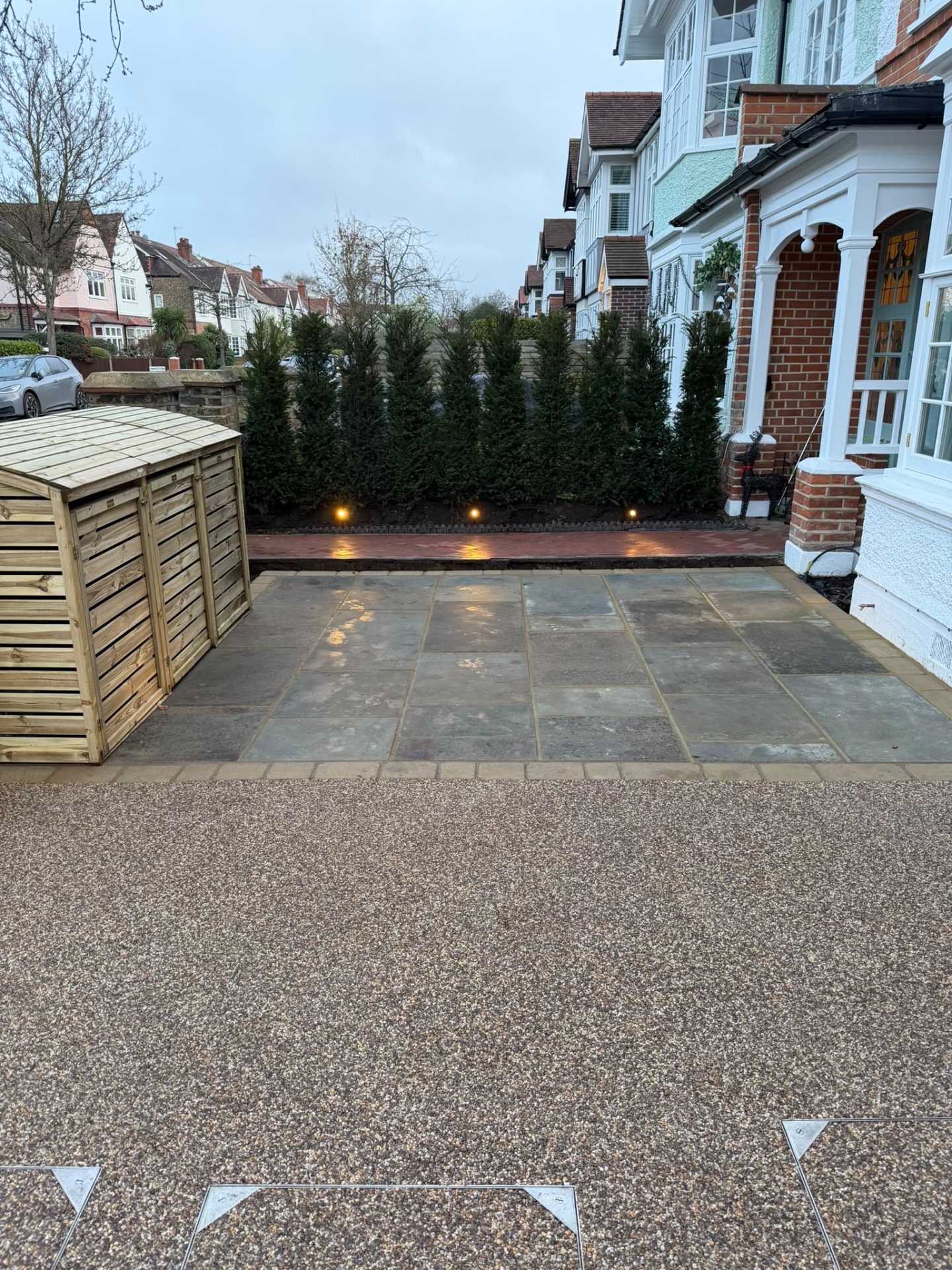Resin-bound driveway and yorkstone paving at dusk, with low uplights along the evergreen screen