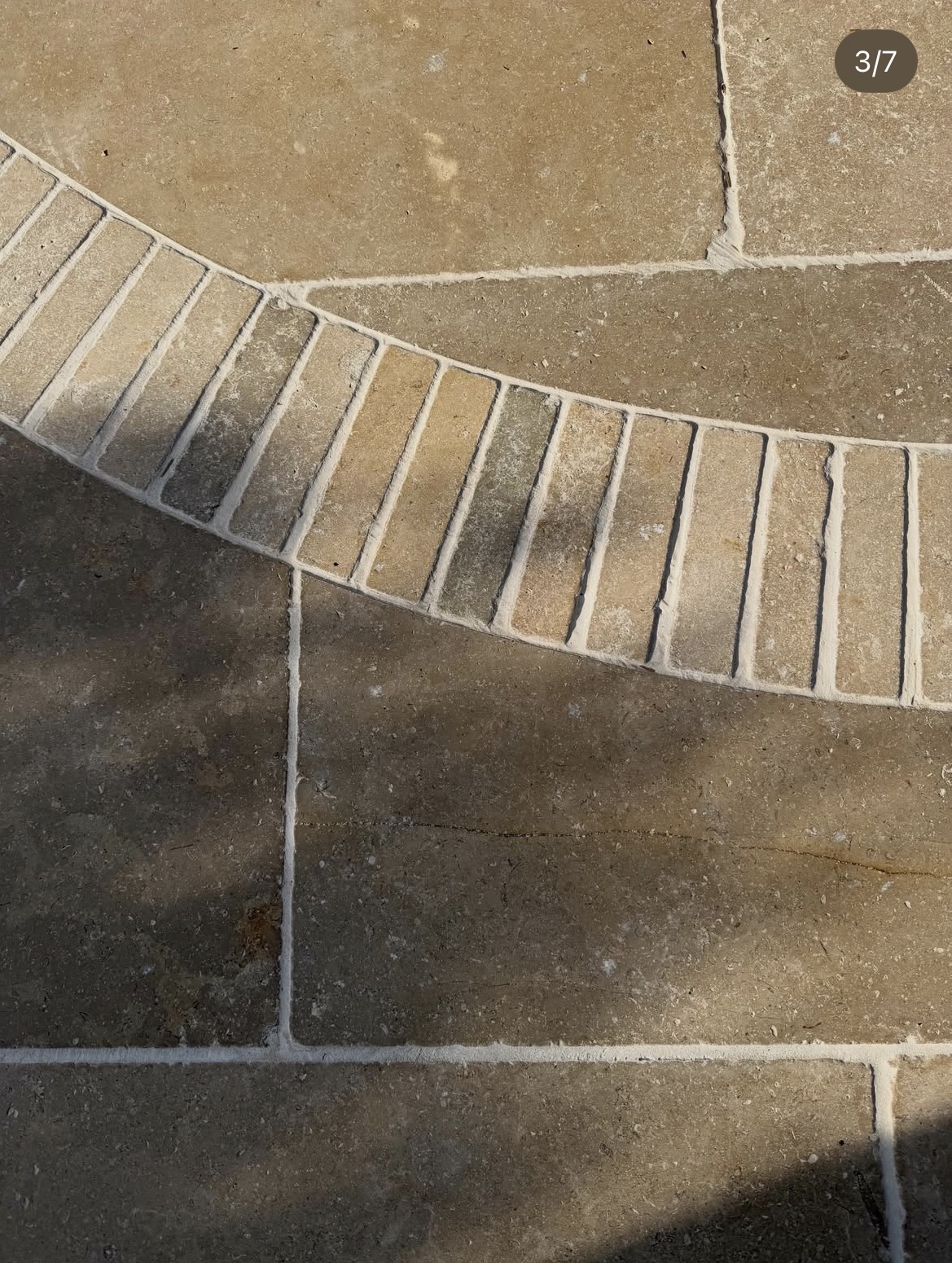 Close detail of clay pavers forming a curved band through natural stone paving