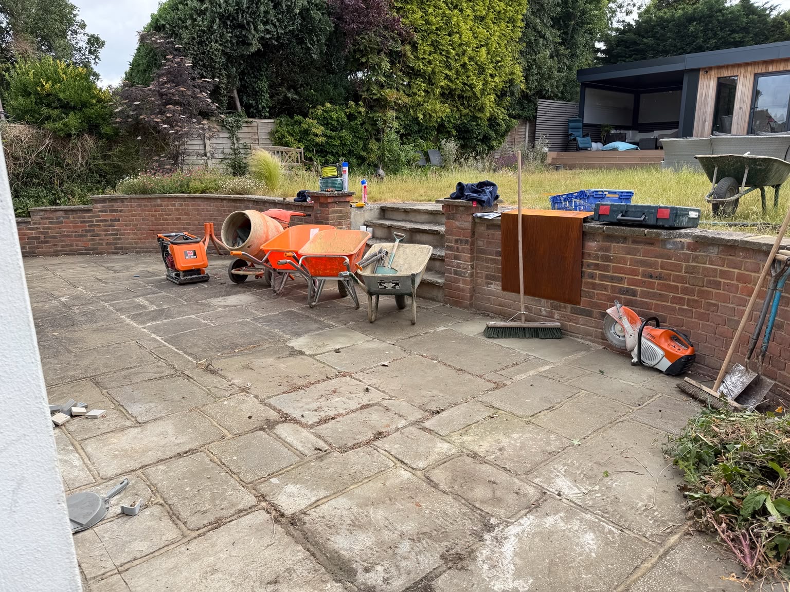 The original worn sandstone patio and curved brick retaining wall as work began, with a corten steel sample on the wall