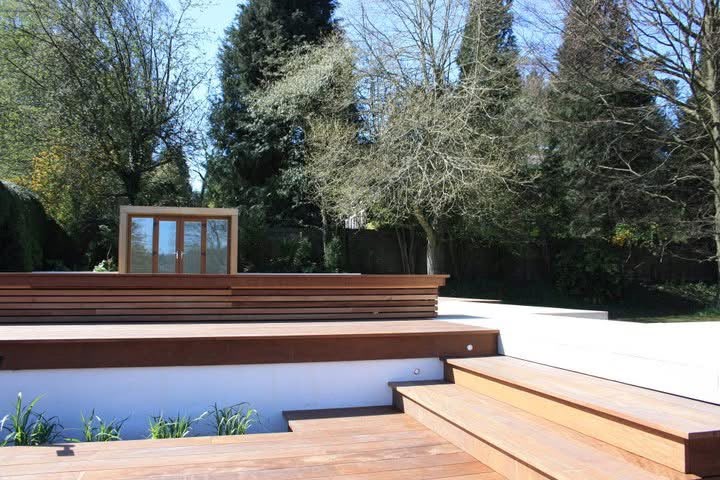 Completed hardwood decking across the sloped garden with wide steps up to a sandstone terrace, a white retaining wall with recessed lights and the timber garden room