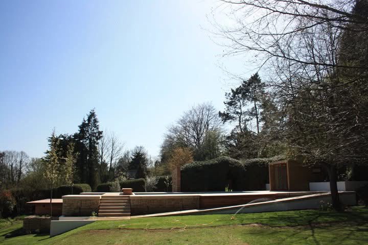 Wide view of the finished terraced hillside, with gabion cages, sandstone steps, the renovated pool and garden building