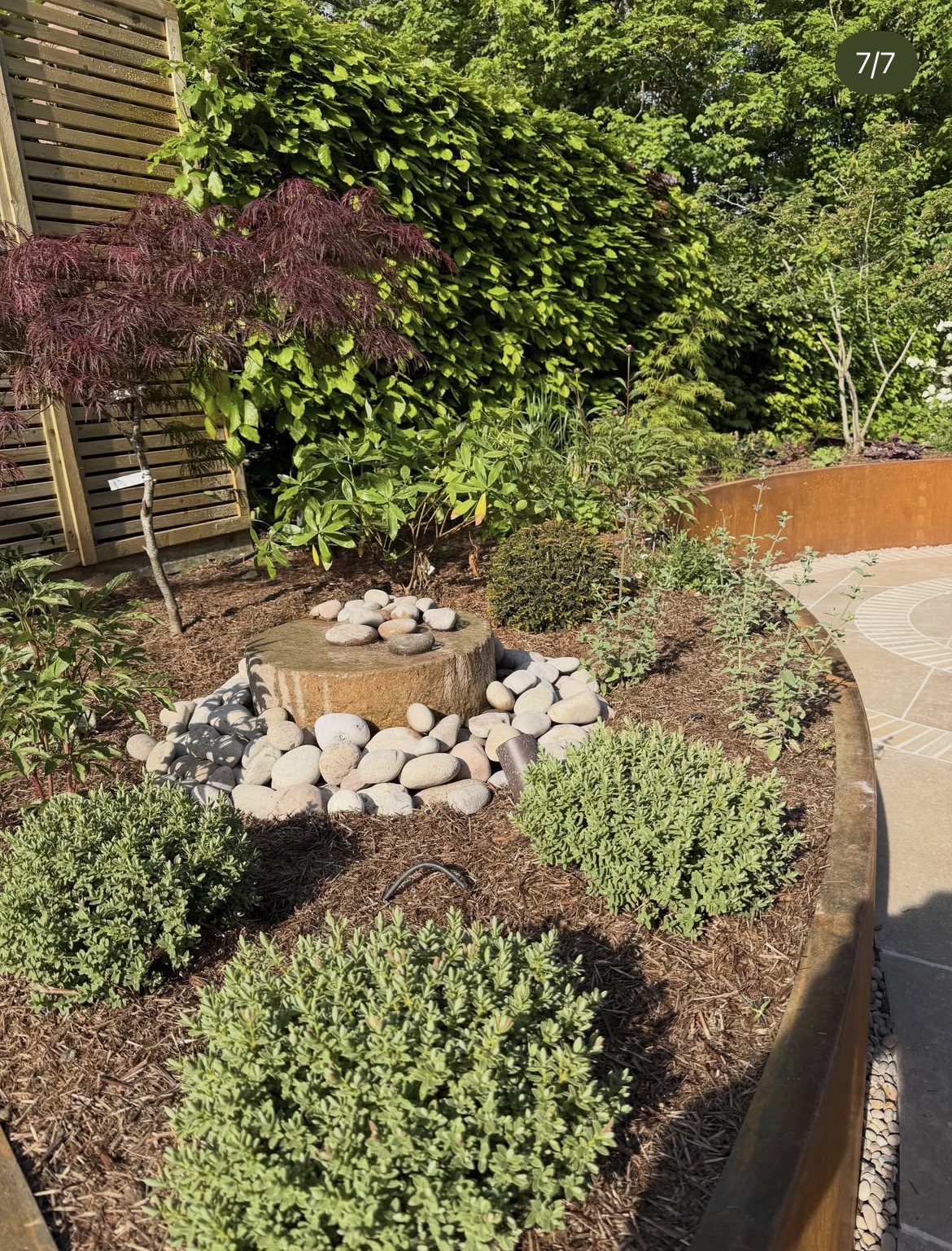Layered planting and stone arrangement within the curved corten garden
