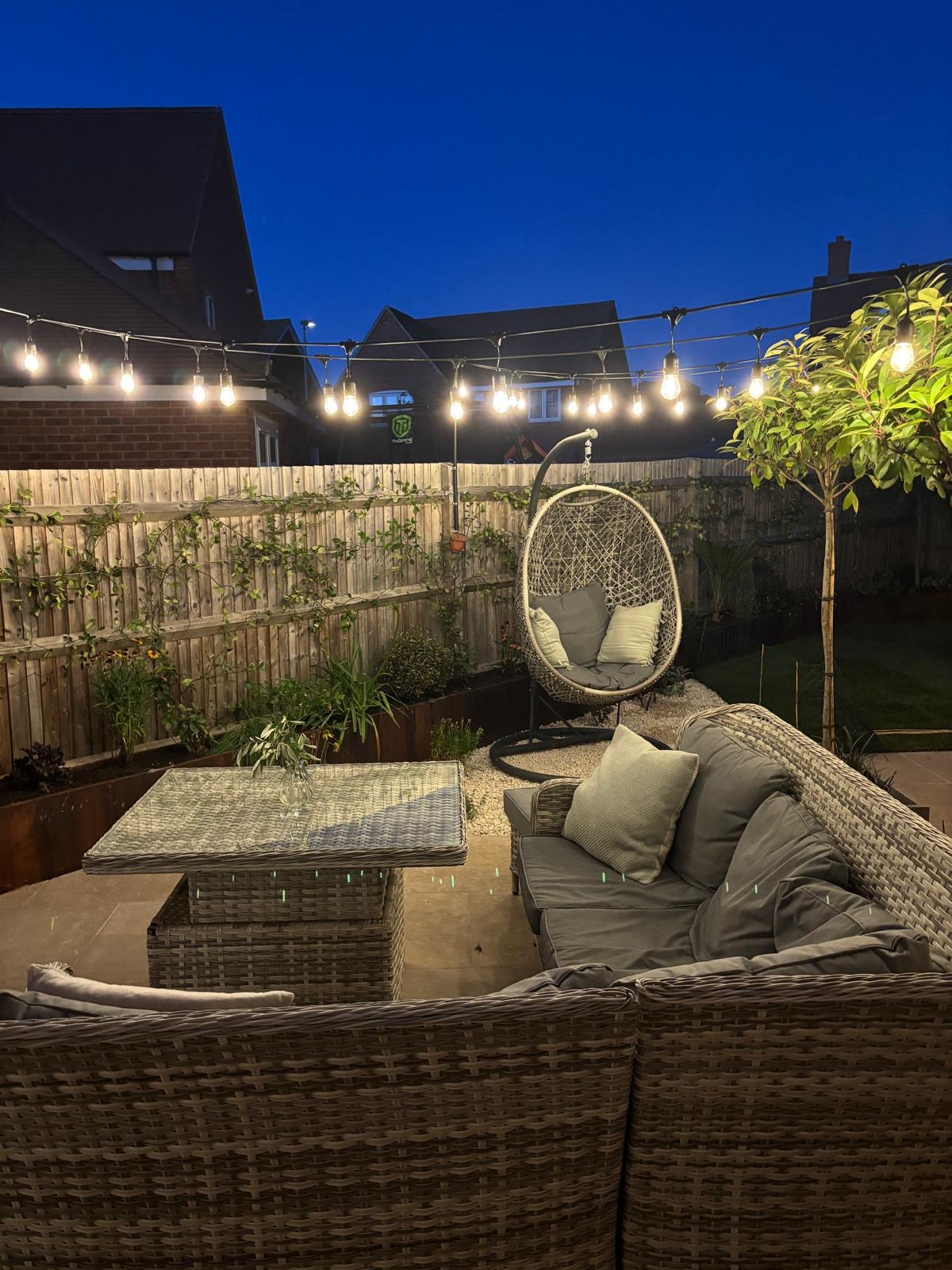 Lower-angle view of the wicker seating and hanging egg chair at twilight under festoon lighting