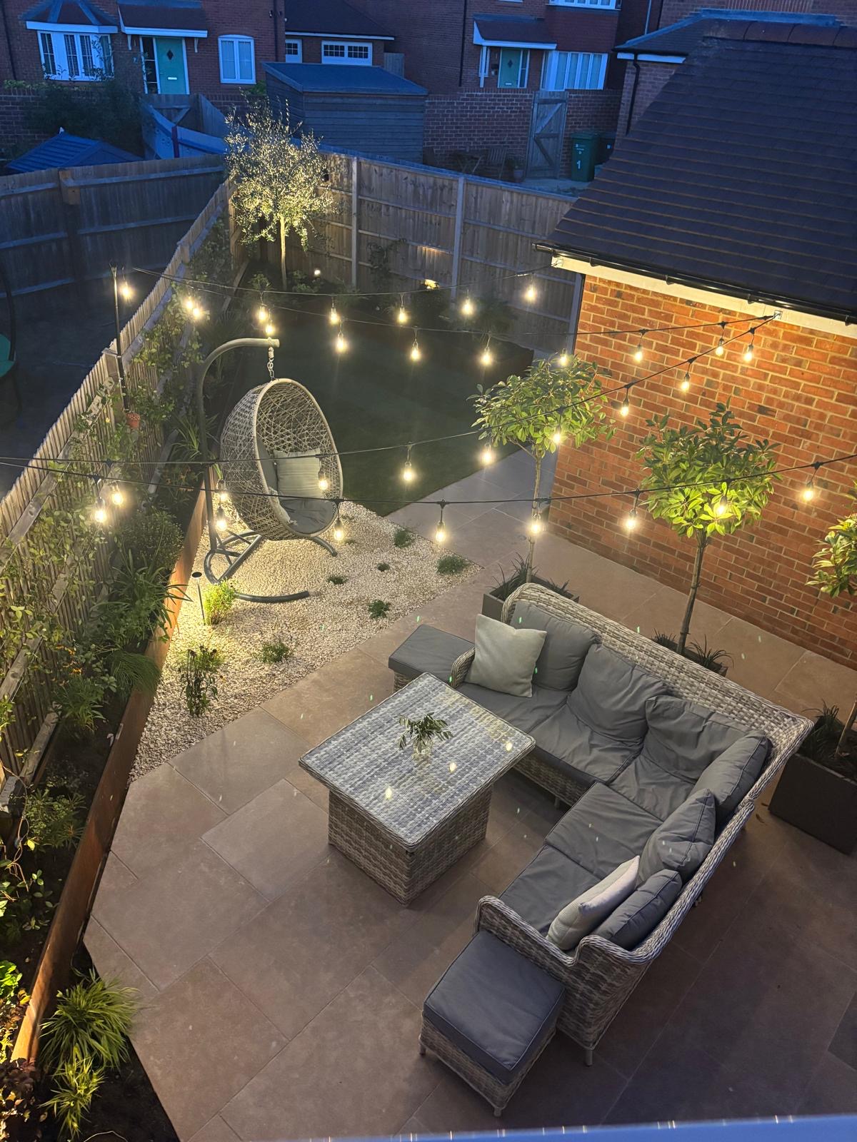 Garden at twilight with festoon lights glowing above the patio, gravel area and corten steel planters