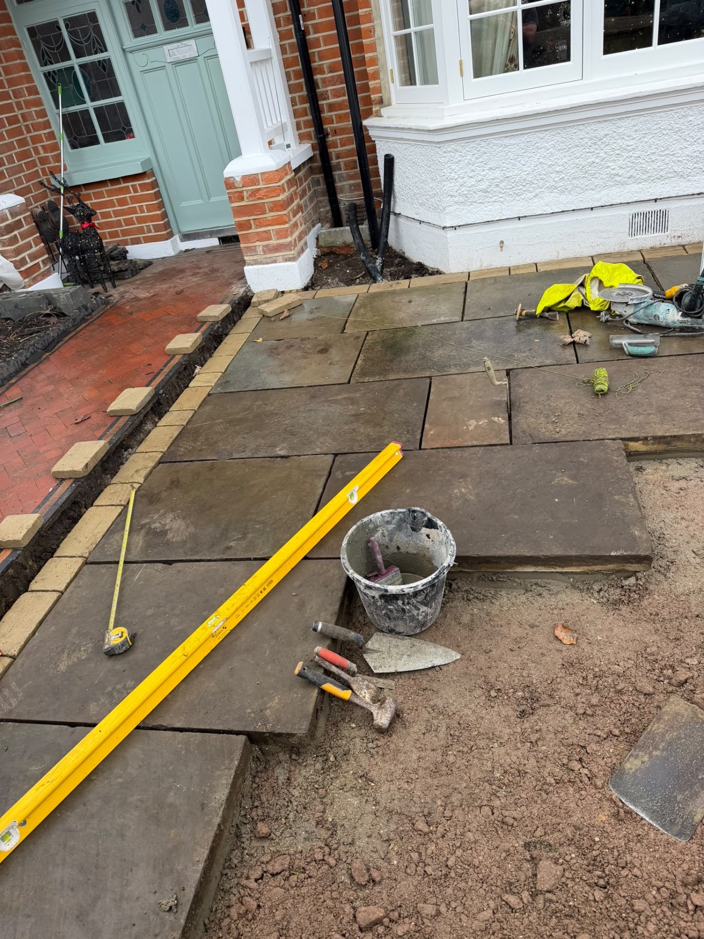 Yorkstone flagstones being laid and levelled beside the brick house during construction