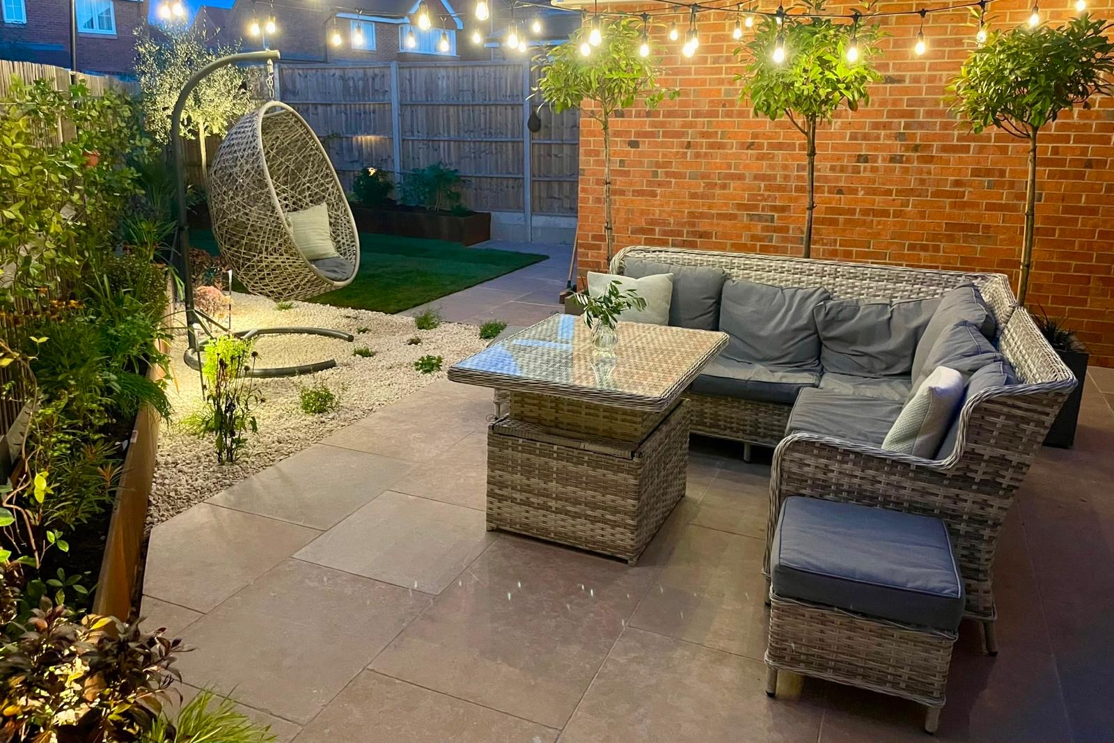 Garden at night lit by festoon lights and low-level uplighting across the planting and seating area