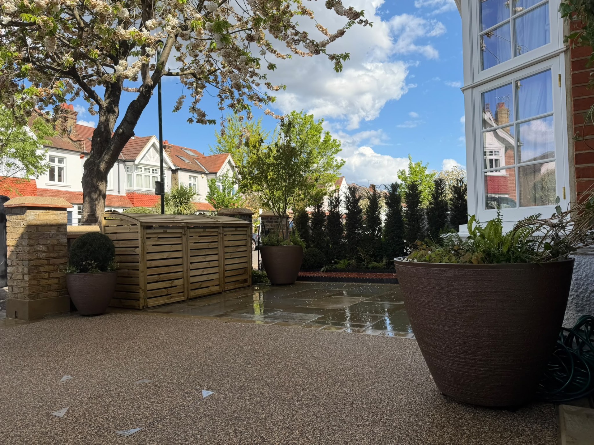 Low view across the finished resin-bound driveway and yorkstone paving to Torc pots and the evergreen screen