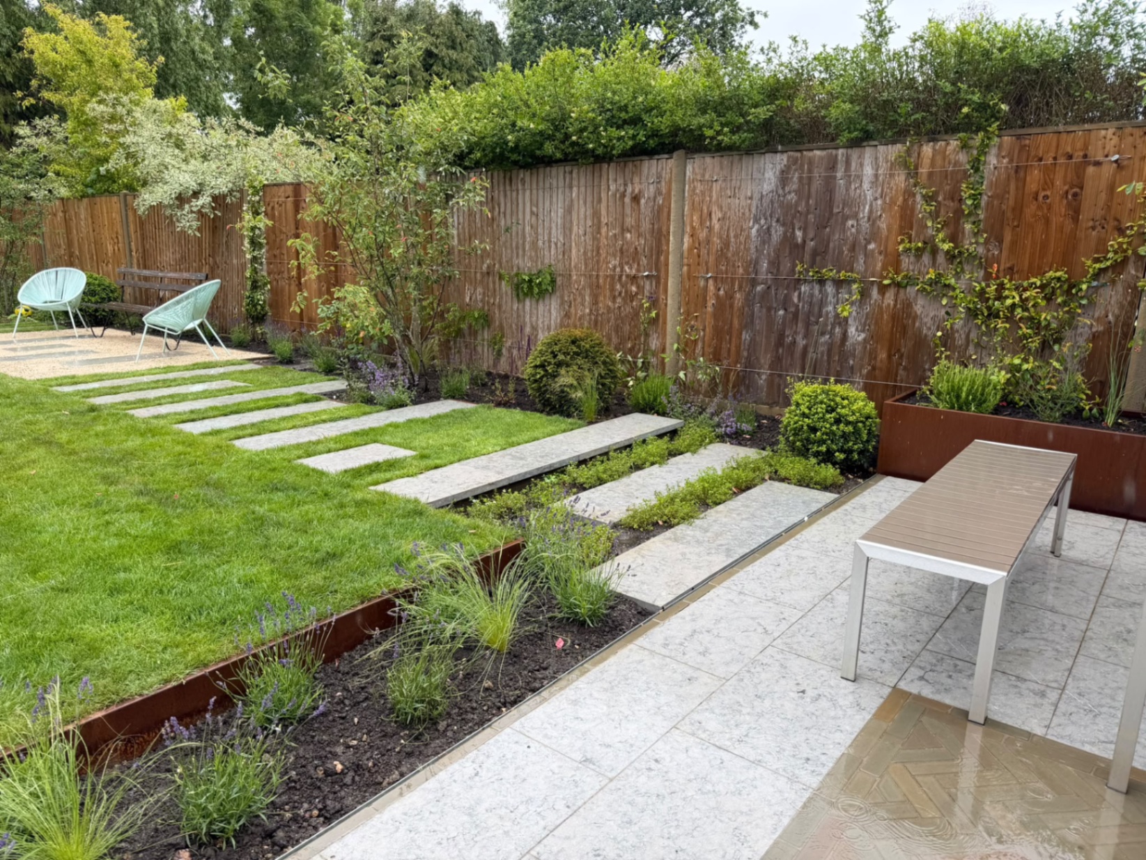 Wide view across the limestone patio towards a raised corten steel planter and garden bench