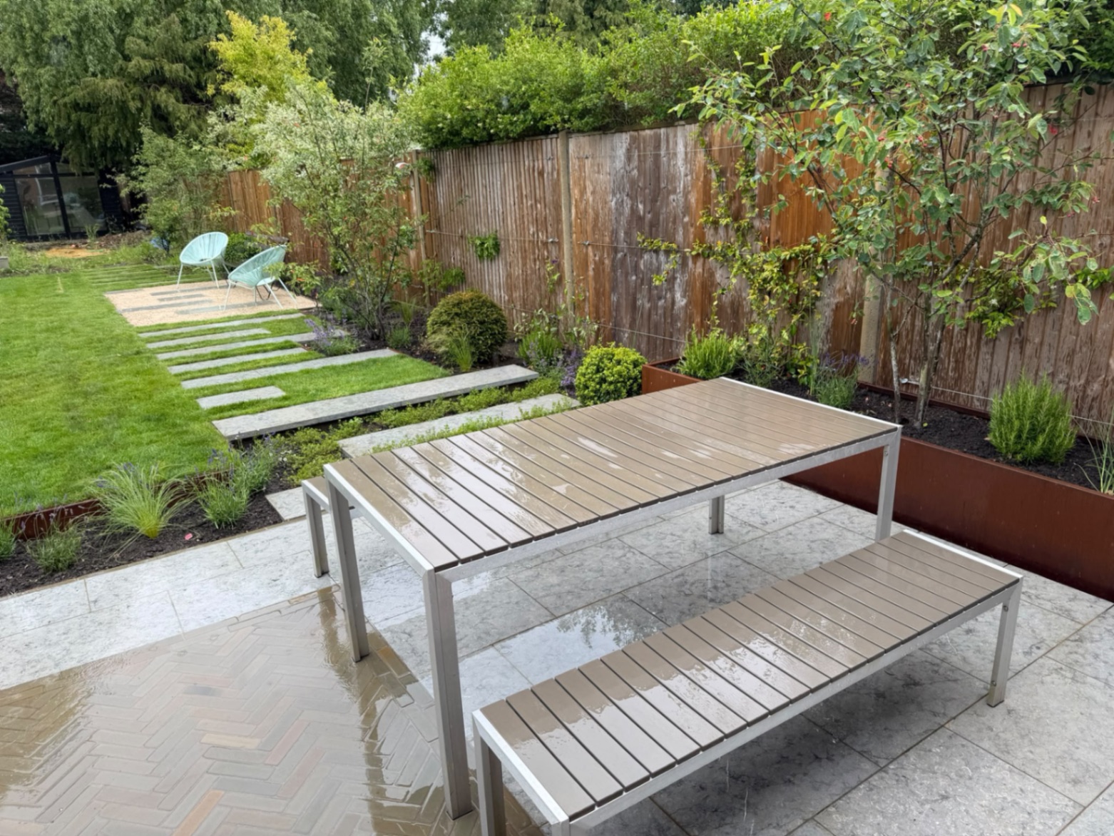 Dining area on the limestone patio beside a tall corten steel trough planter