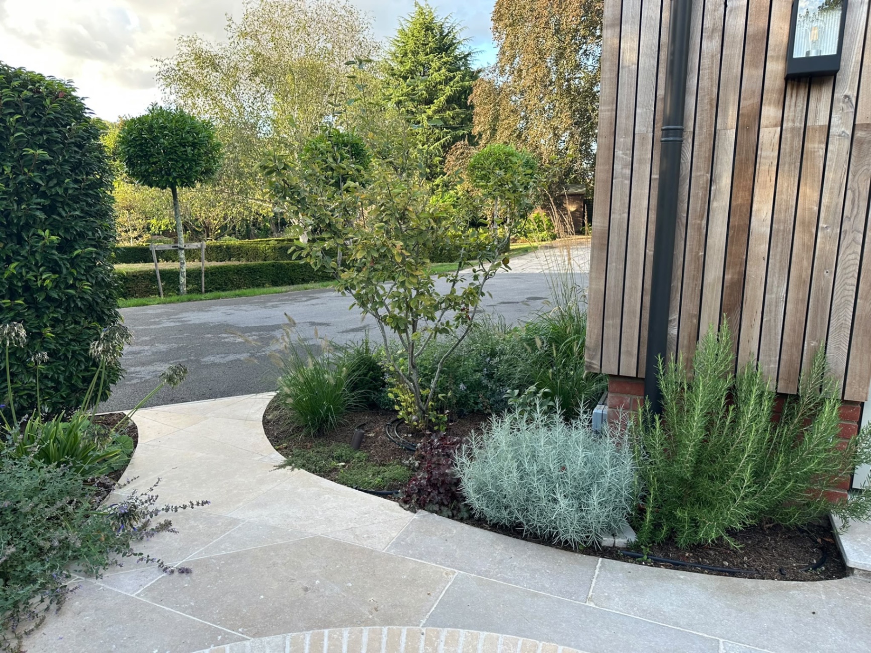 Curved limestone path with brick-inlay border beside a planting bed of lavender, rosemary and heuchera